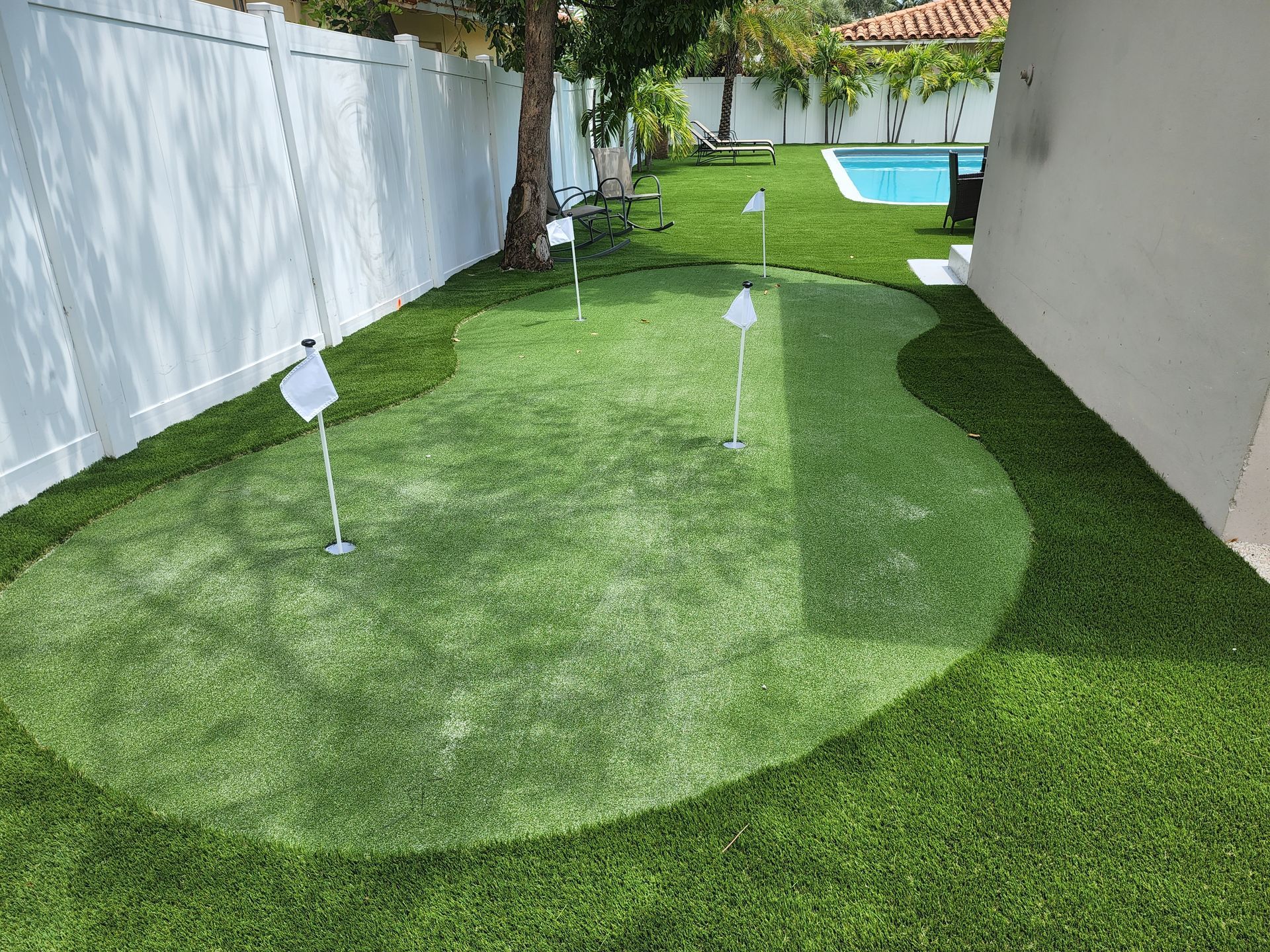 A putting green in a backyard next to a pool.