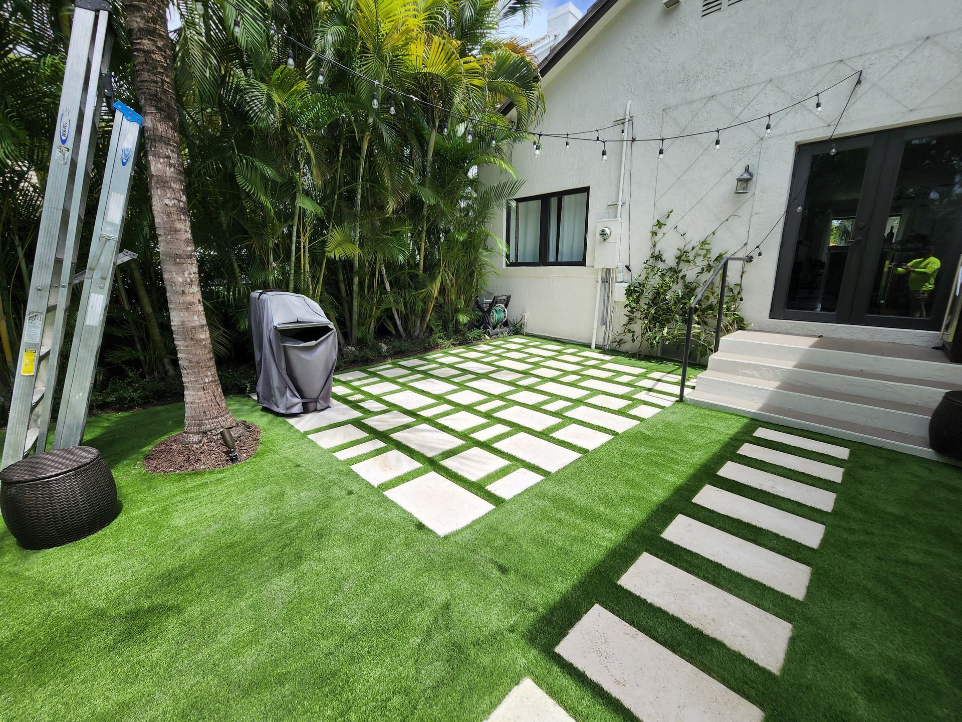 A white house with a lawn and a ladder in front of it.