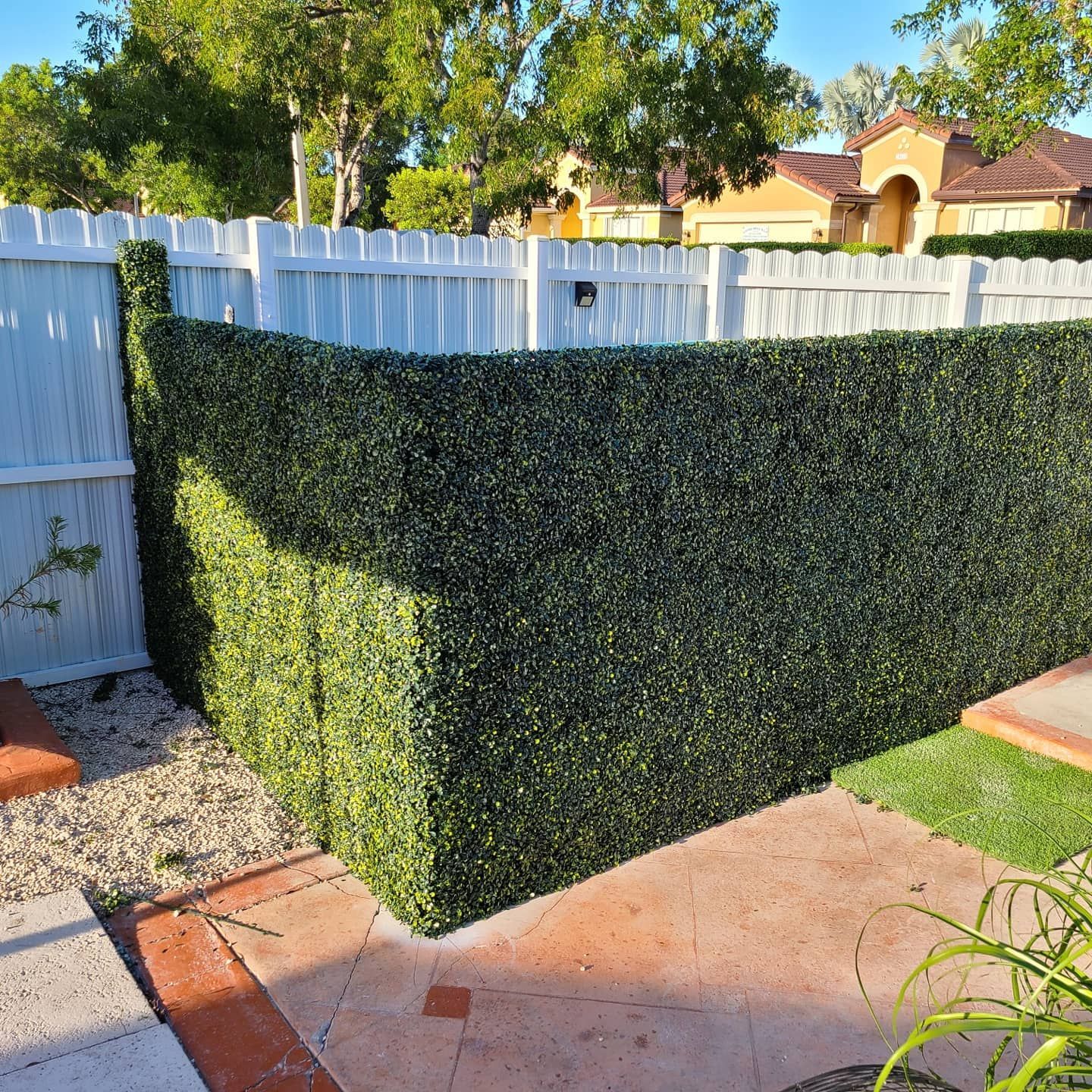 A white fence is surrounded by a green hedge.