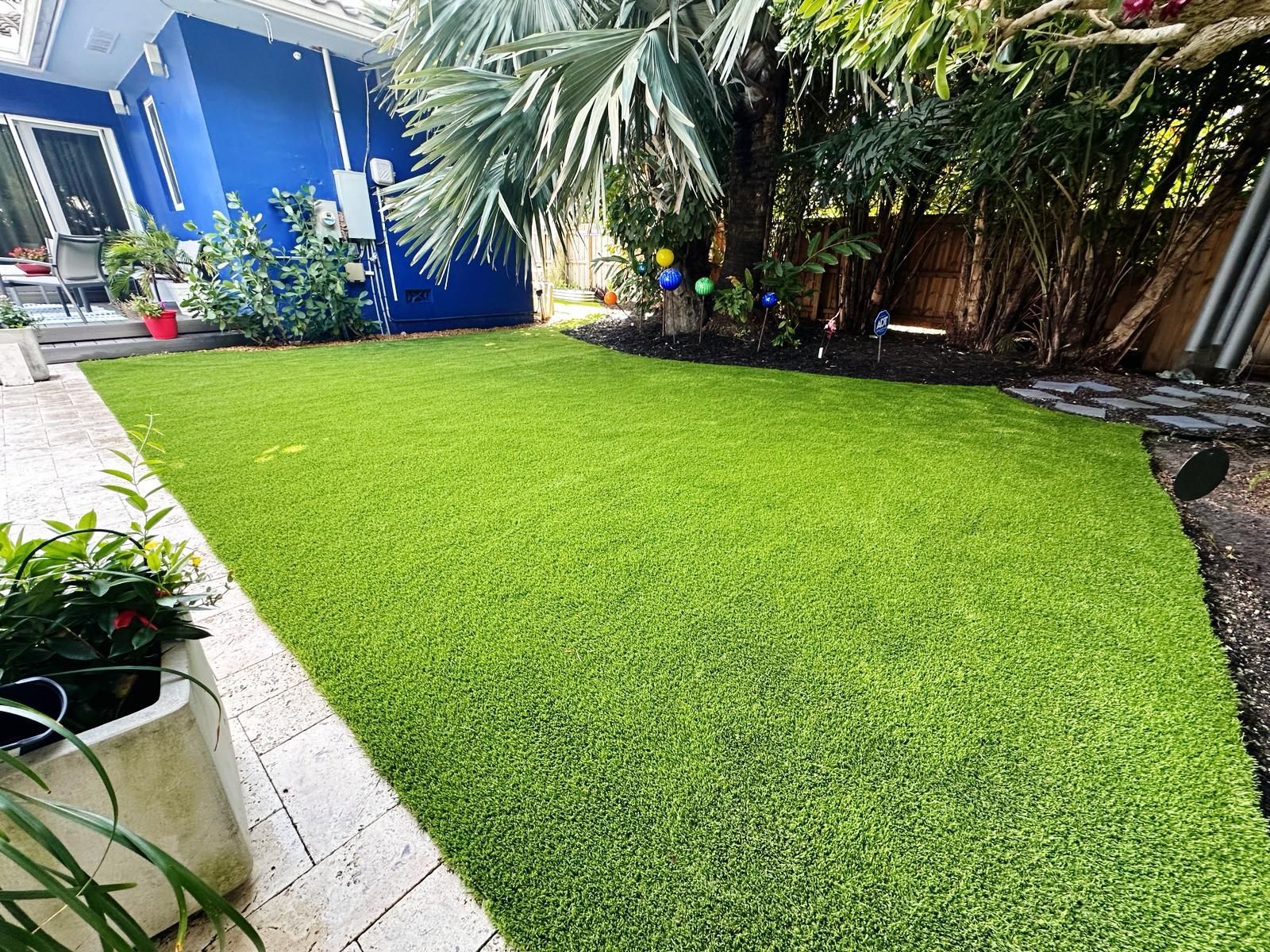 A backyard with a lush green lawn and a blue house in the background.