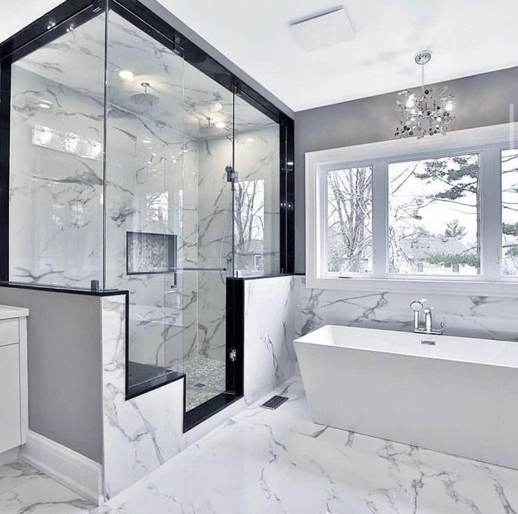Modern white bathroom with marble tile, glass shower enclosure, freestanding tub, and large windows