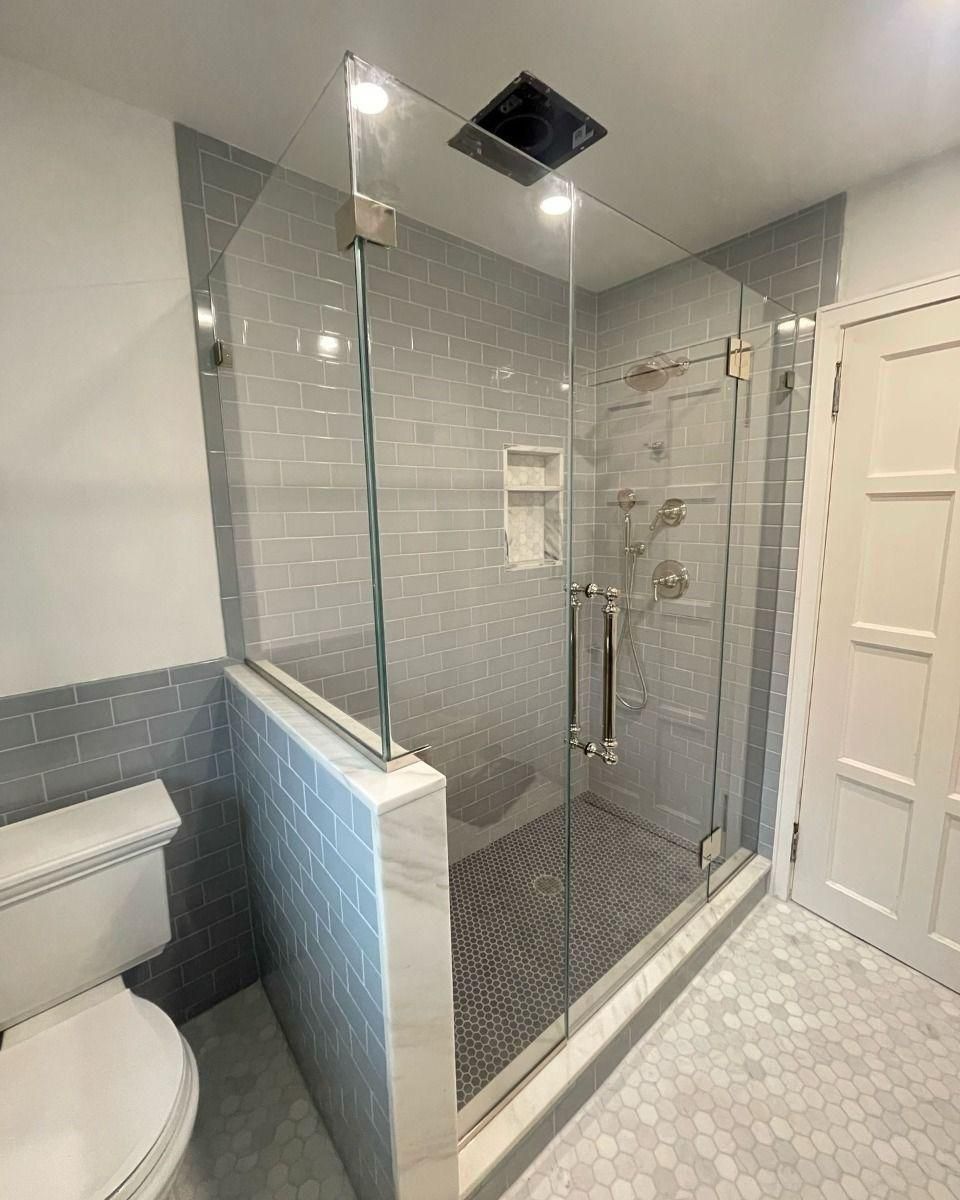 Modern bathroom with glass shower enclosure, gray tile, and toilet visible on the left.