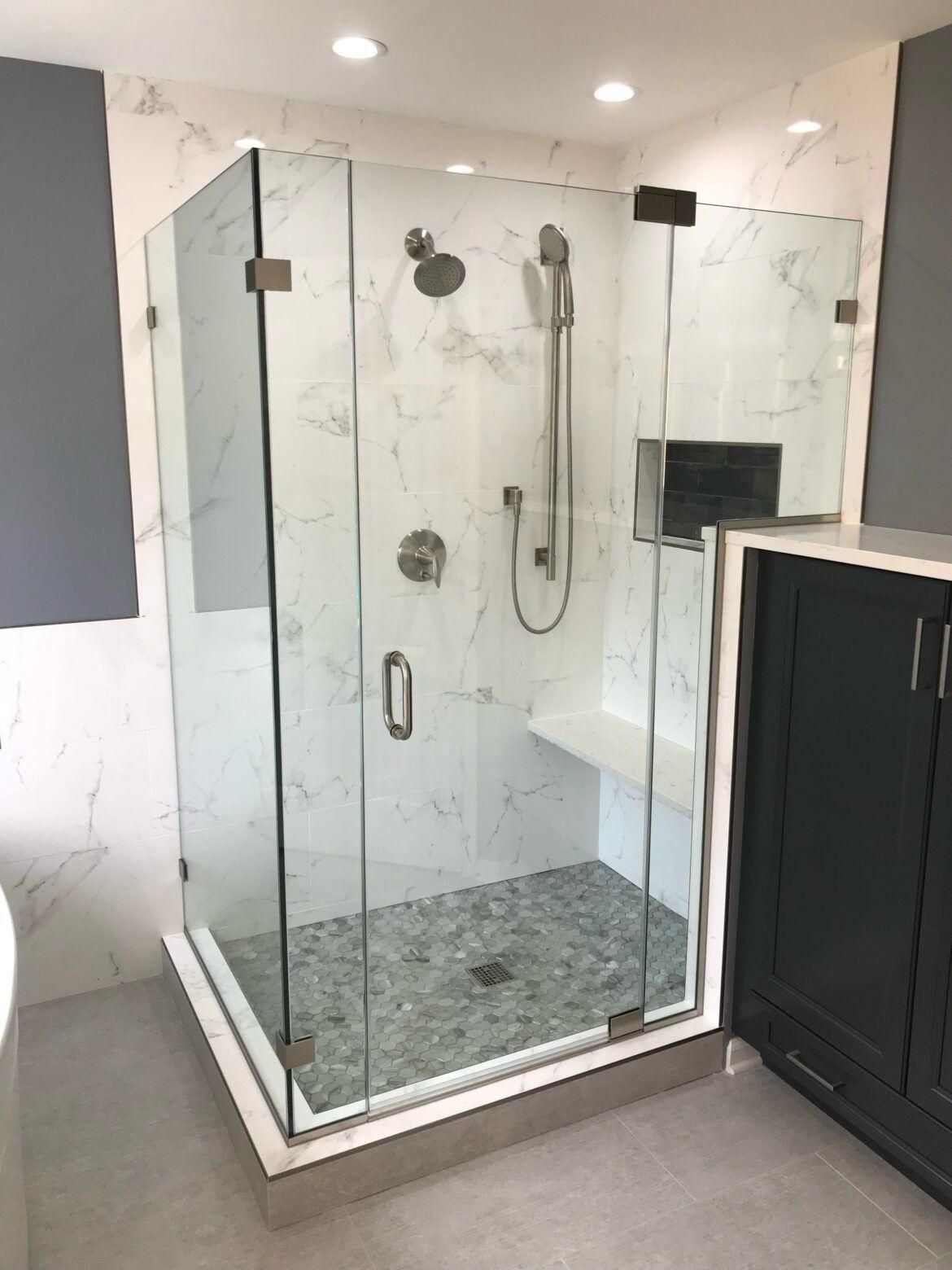 Modern bathroom with glass walk-in shower, marble walls, and dark vanity cabinet