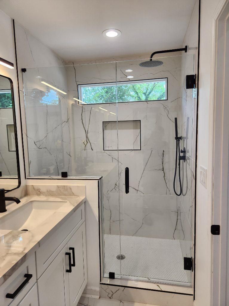 Modern bathroom with marble shower, glass door, floating vanity, and a horizontal window over the shower