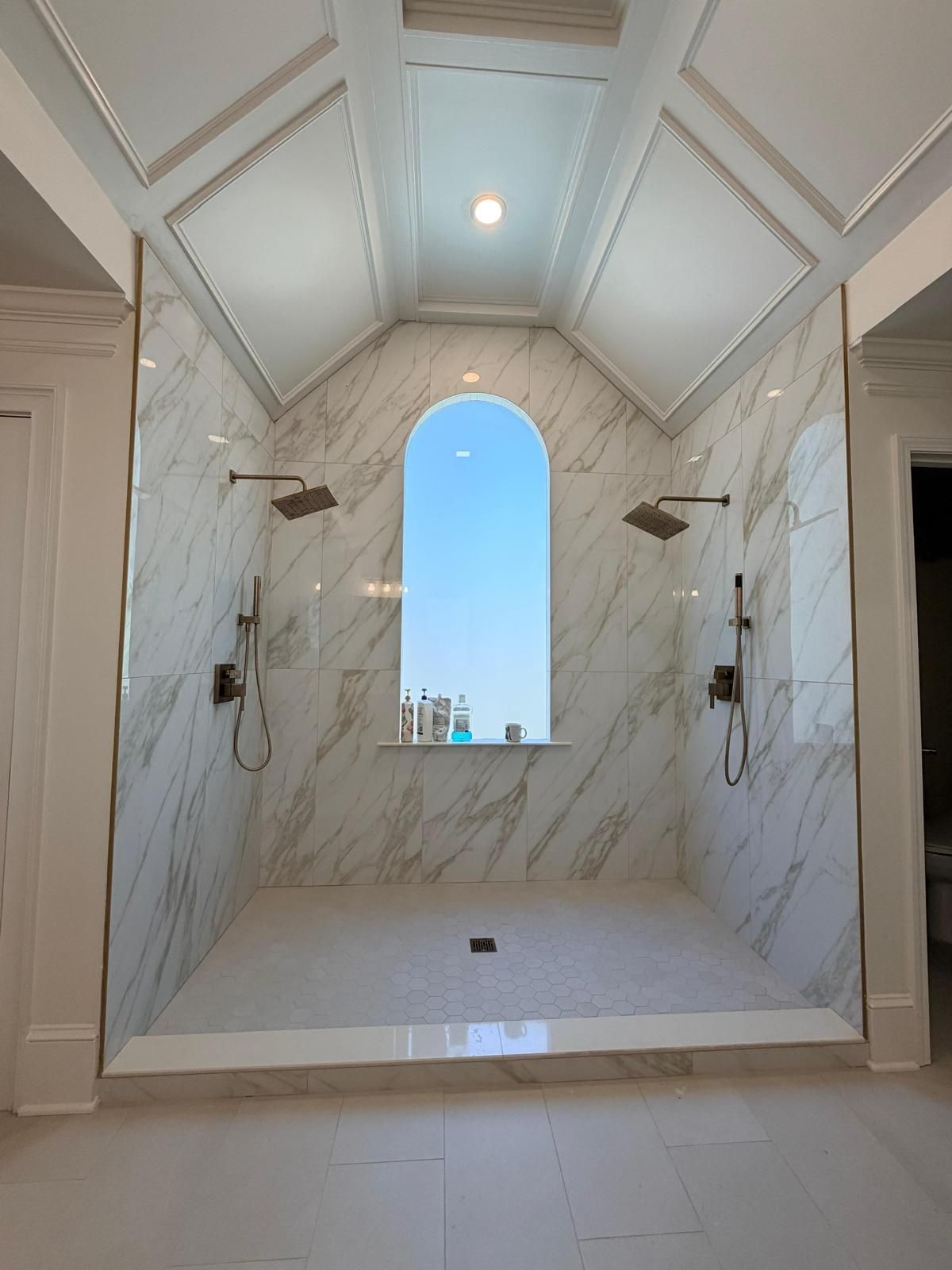 Marble-tiled walk-in shower with arched window and dual wall-mounted showerheads