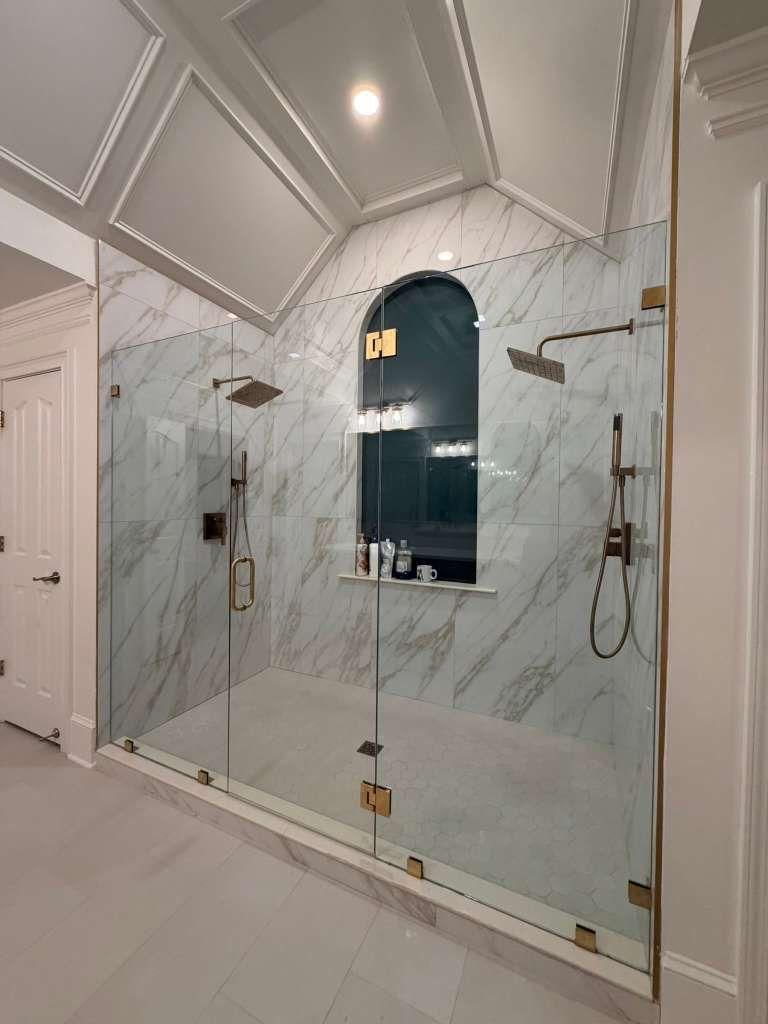 Luxury marble bathroom with a glass-enclosed shower, gold hardware, and arched mirror