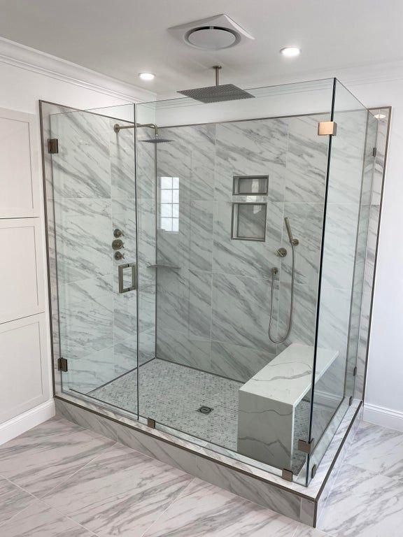 Modern glass-enclosed marble-tiled shower with rain head and built-in bench in a bright bathroom