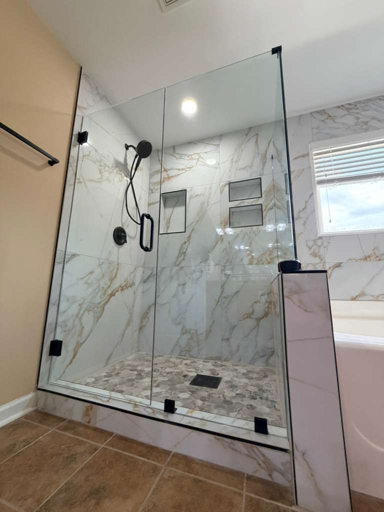 Glass shower with marble-look walls, black fixtures, and tiled floor in a bathroom