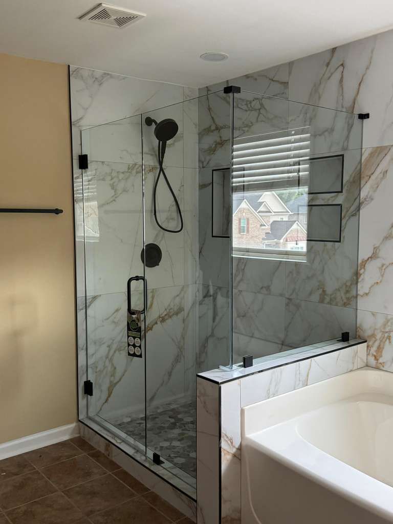 Modern bathroom shower with glass enclosure, marble-look tile, and a white soaking tub.