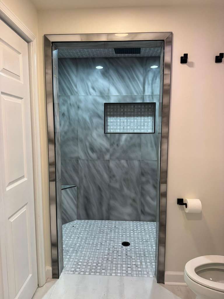 Bathroom shower with gray tile, handheld shower, and white toilet visible beside it