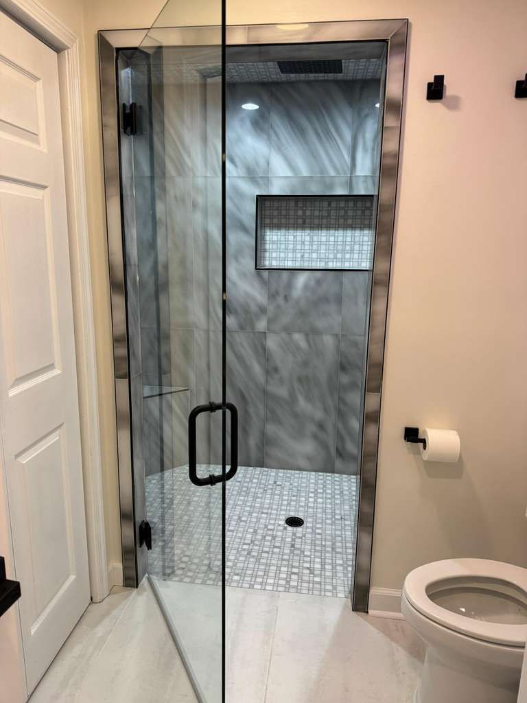 Small bathroom with a glass shower enclosure, white toilet, and gray tiled shower area.