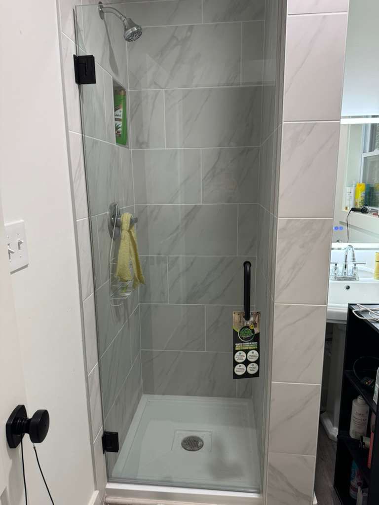 Small tiled shower stall with a handheld showerhead and squeegee hanging on the wall.