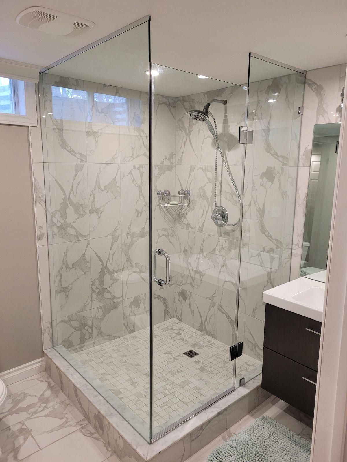 Glass walk-in shower with marble tile walls, chrome fixtures, and a shower bench beside a vanity sink.