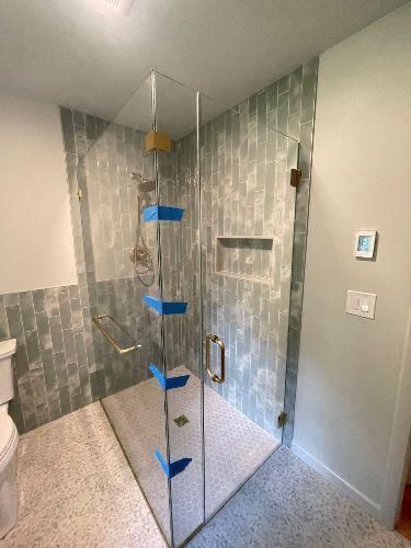 Glass walk-in shower with gray tile walls and blue tape marking the glass panel