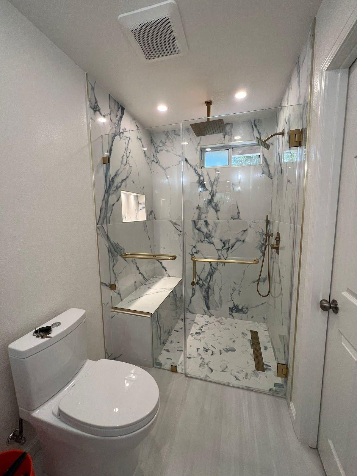 Modern accessible bathroom with toilet, roll-in shower, marble walls, and grab bars