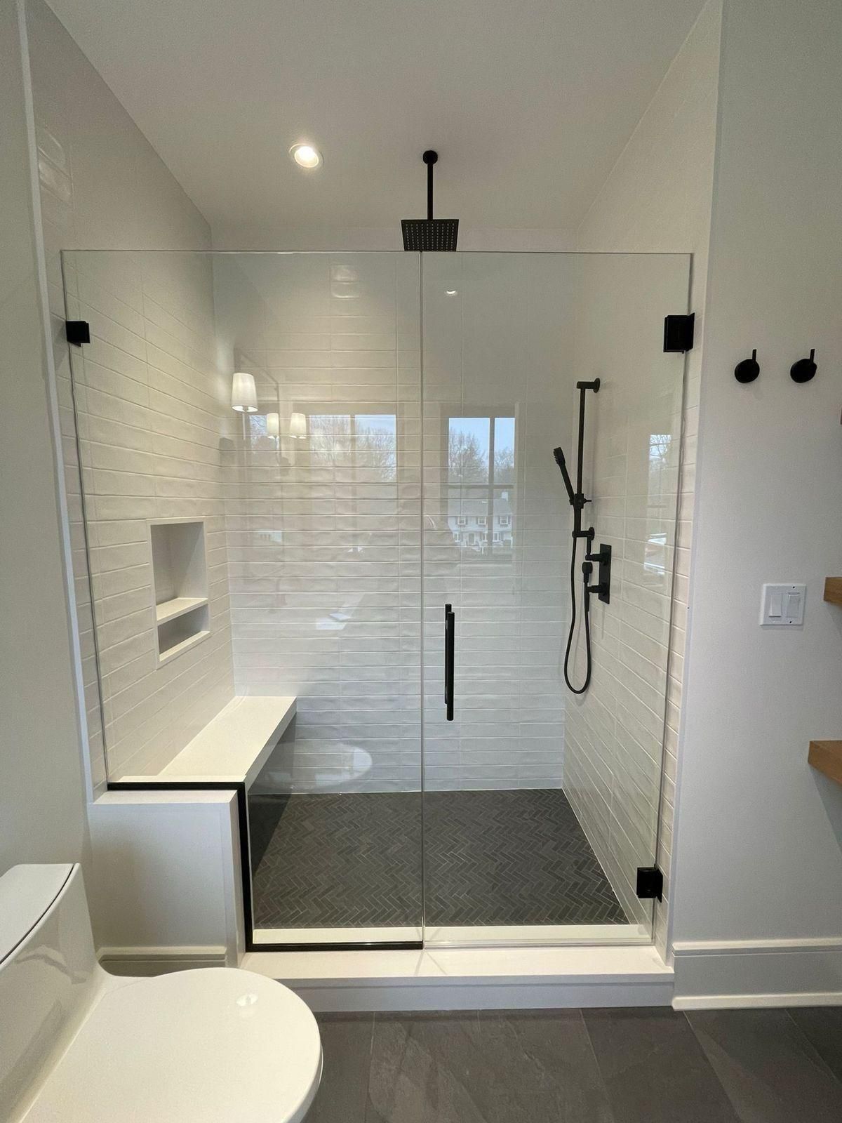 Modern white walk-in shower with glass door, bench, and black fixtures in a bathroom