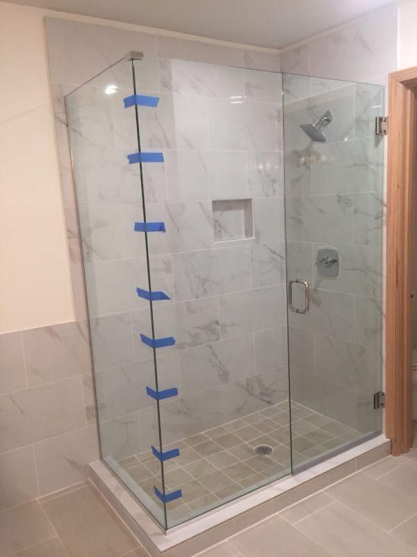 Glass corner shower enclosure with blue tape on the left edge, in a tiled bathroom.