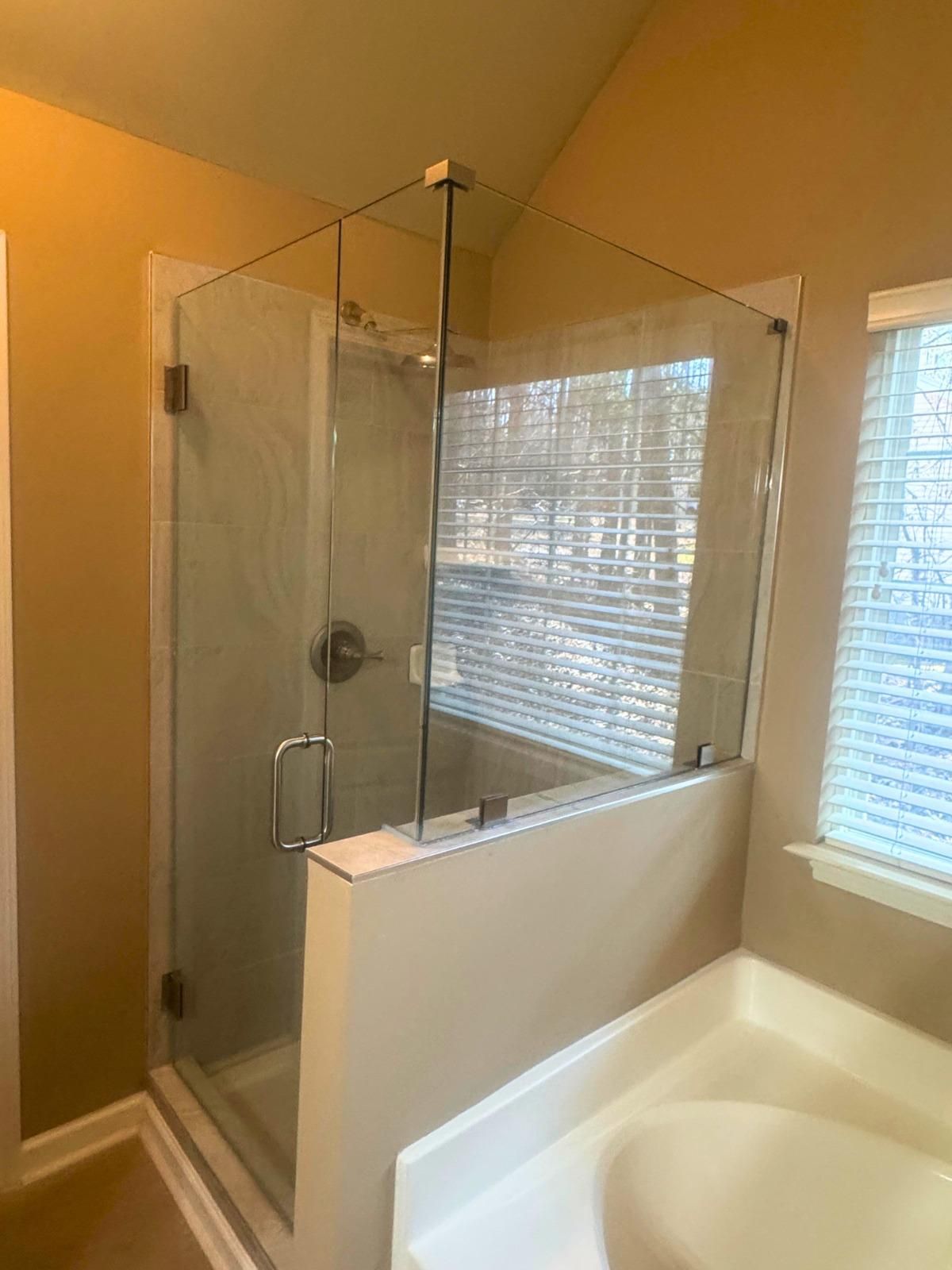 Bathroom with glass-enclosed shower beside a white soaking tub and window blinds