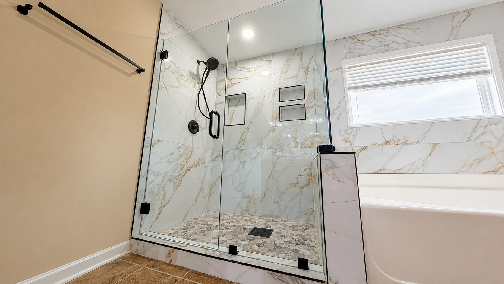 Bathroom with marble shower wall, glass door, and a white bathtub under a window.