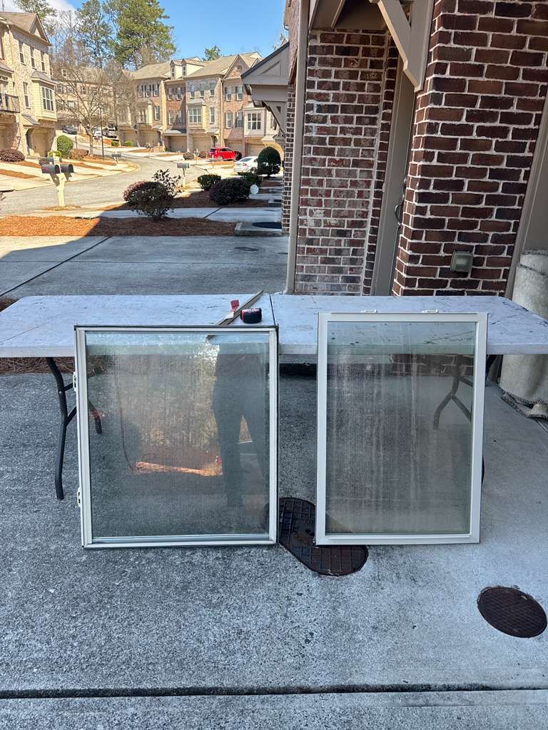 Two white window screens leaning against a brick porch wall on a concrete driveway