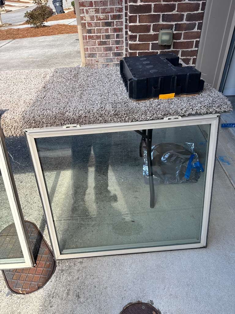 Glass storm door leaning against a brick wall with a black storage bin on top and a blue hose inside