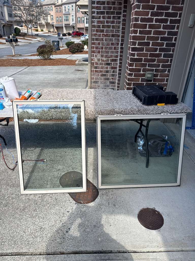 Two glass-framed windows leaning against a brick wall on a sidewalk near a street corner.