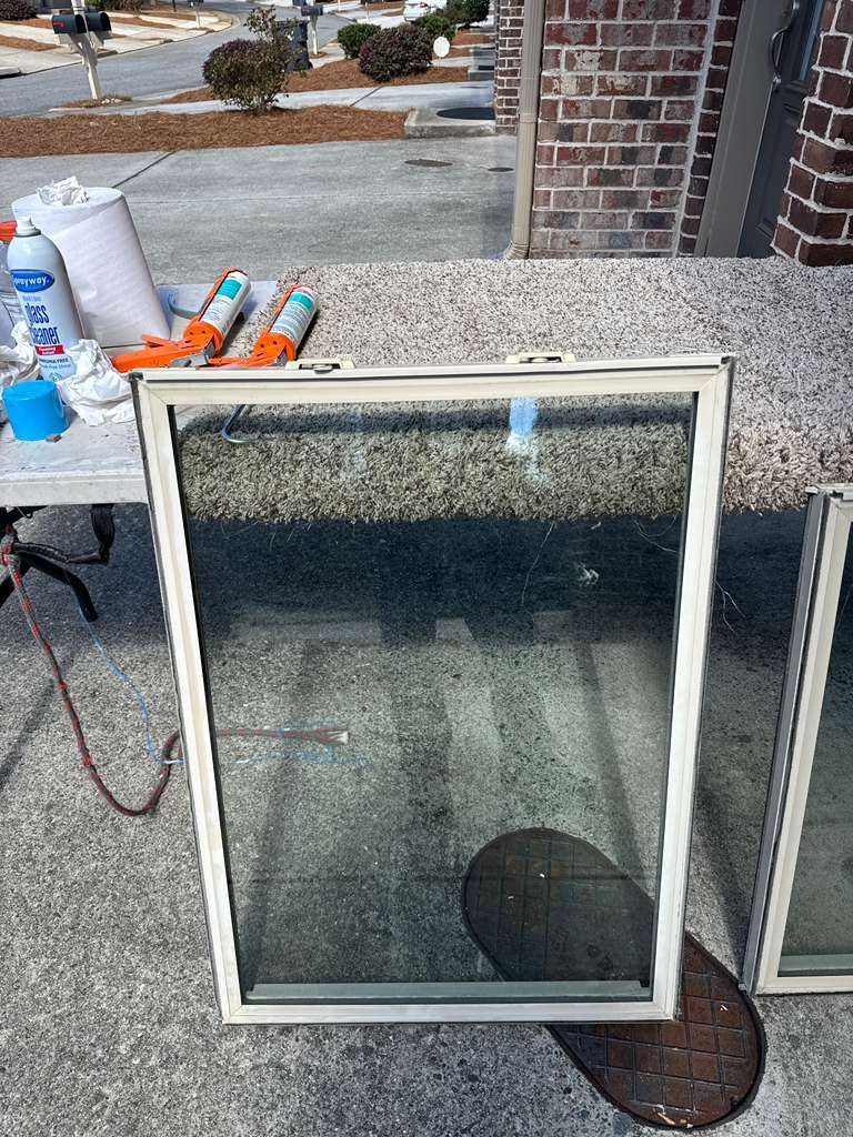 Broken window pane leaning against a brick wall beside a table with spray cans and cleaning supplies