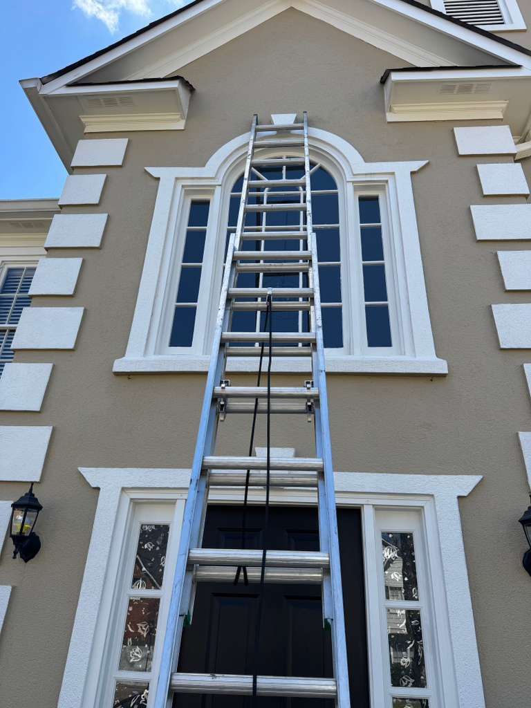 Ladder leaning against a beige house, reaching up to the upper window.