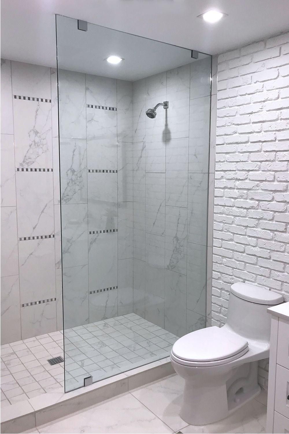 Modern bathroom with glass shower enclosure, white toilet, and white tiled walls.
