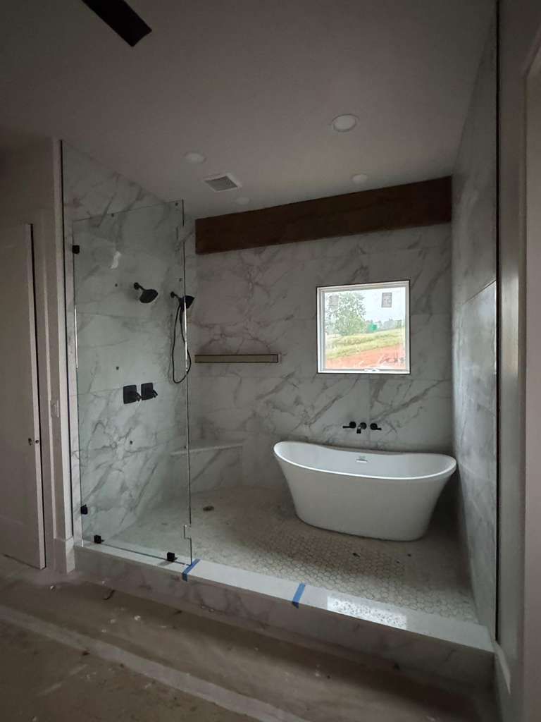 Unfinished bathroom with tiled shower, freestanding tub, and a small window.