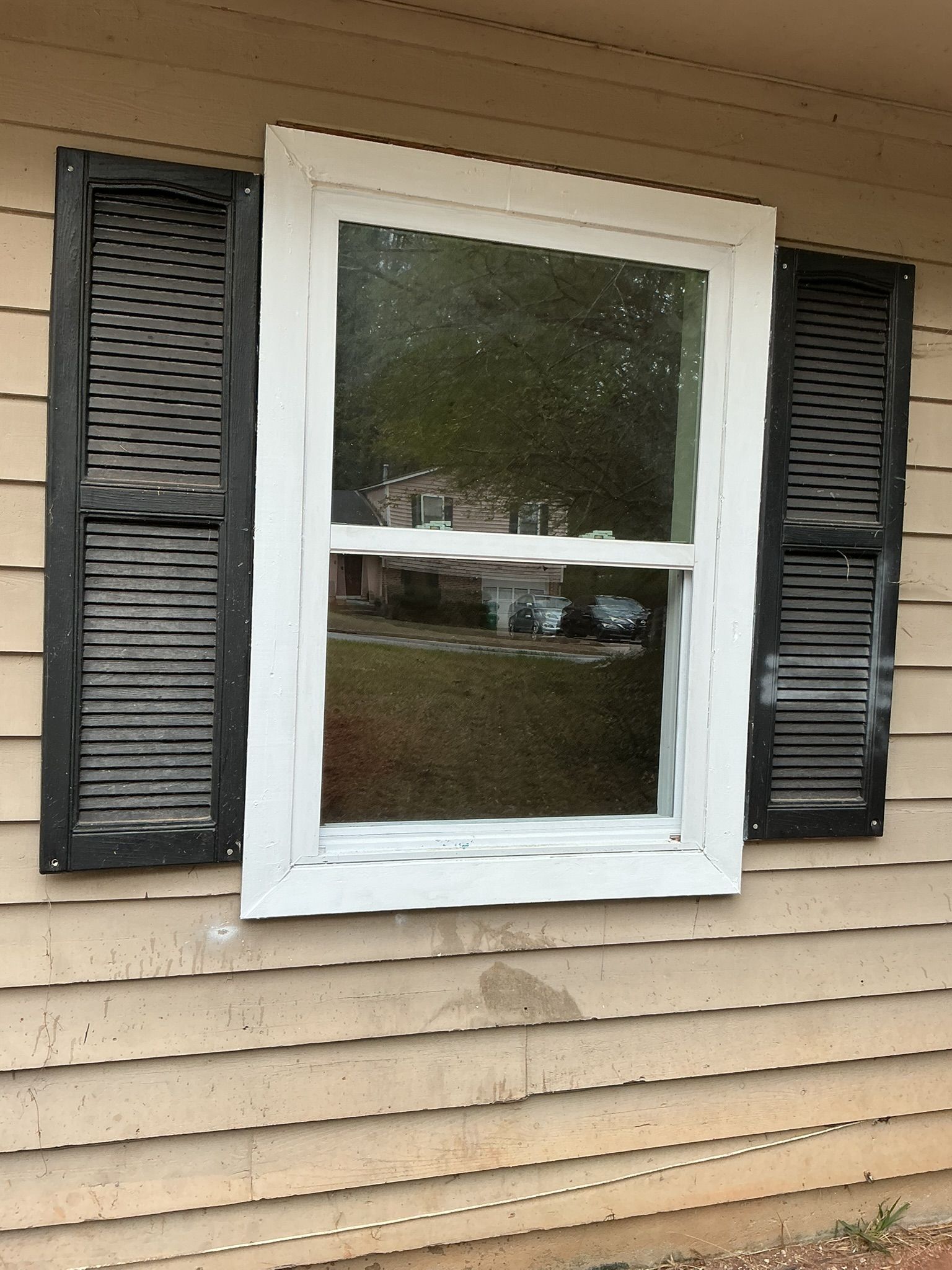 White window with black shutters on tan house siding