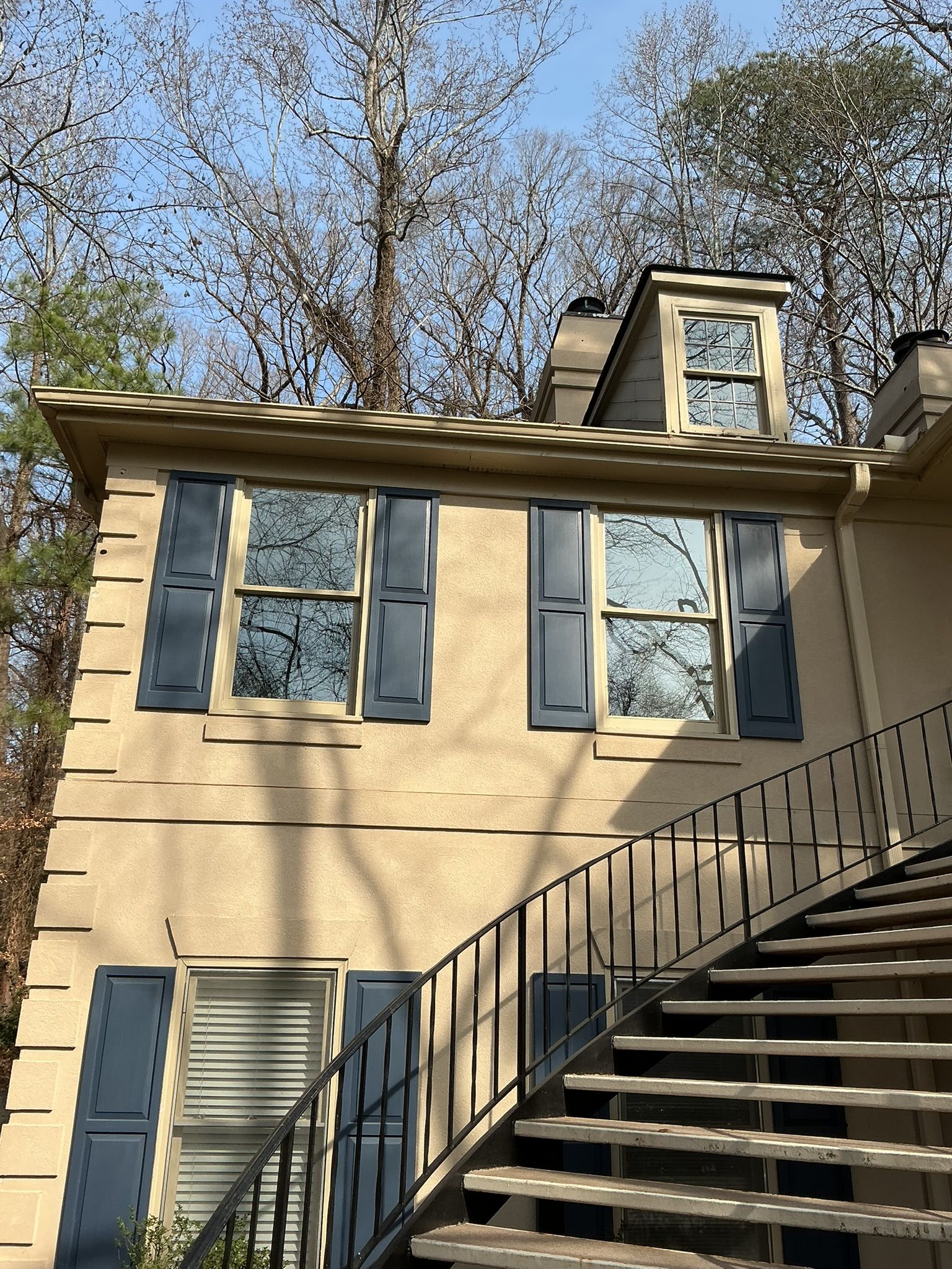 Beige house exterior with dormer windows and a black metal staircase in front.