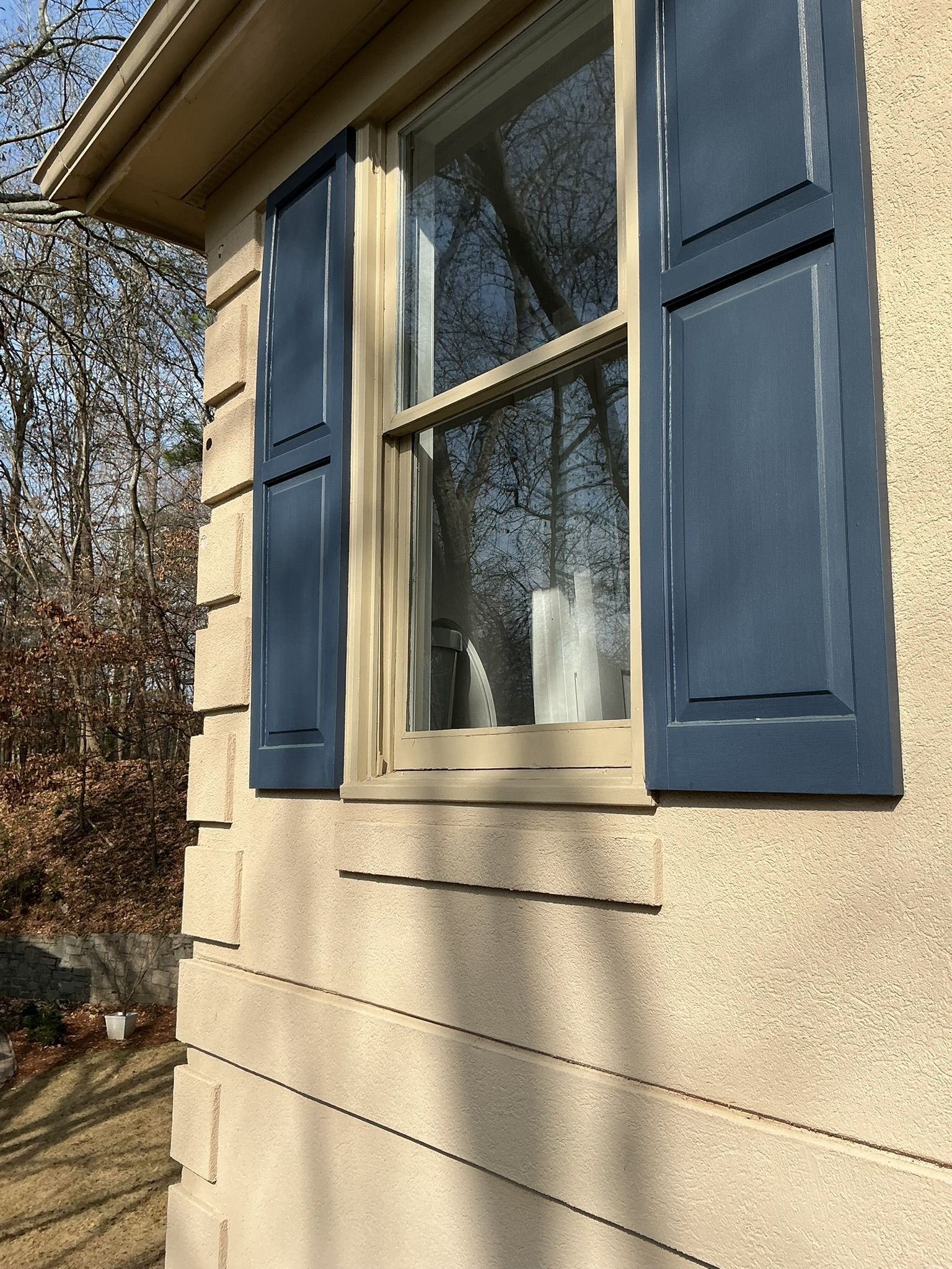 House window with blue shutters on beige siding in daylight