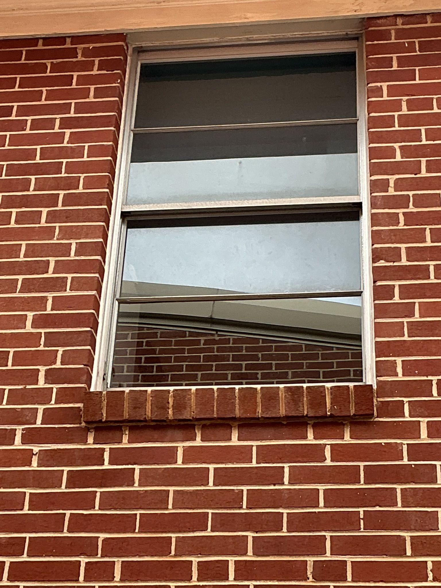 Broken window on a red brick building with cracked glass and a bent frame