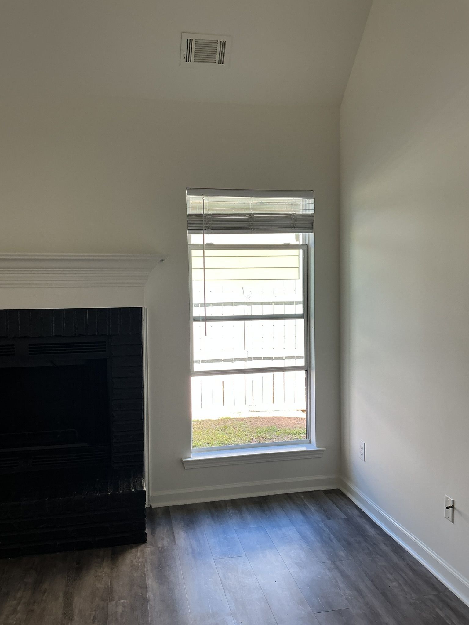 Empty room with white walls, wood floor, a window, and a black fireplace.