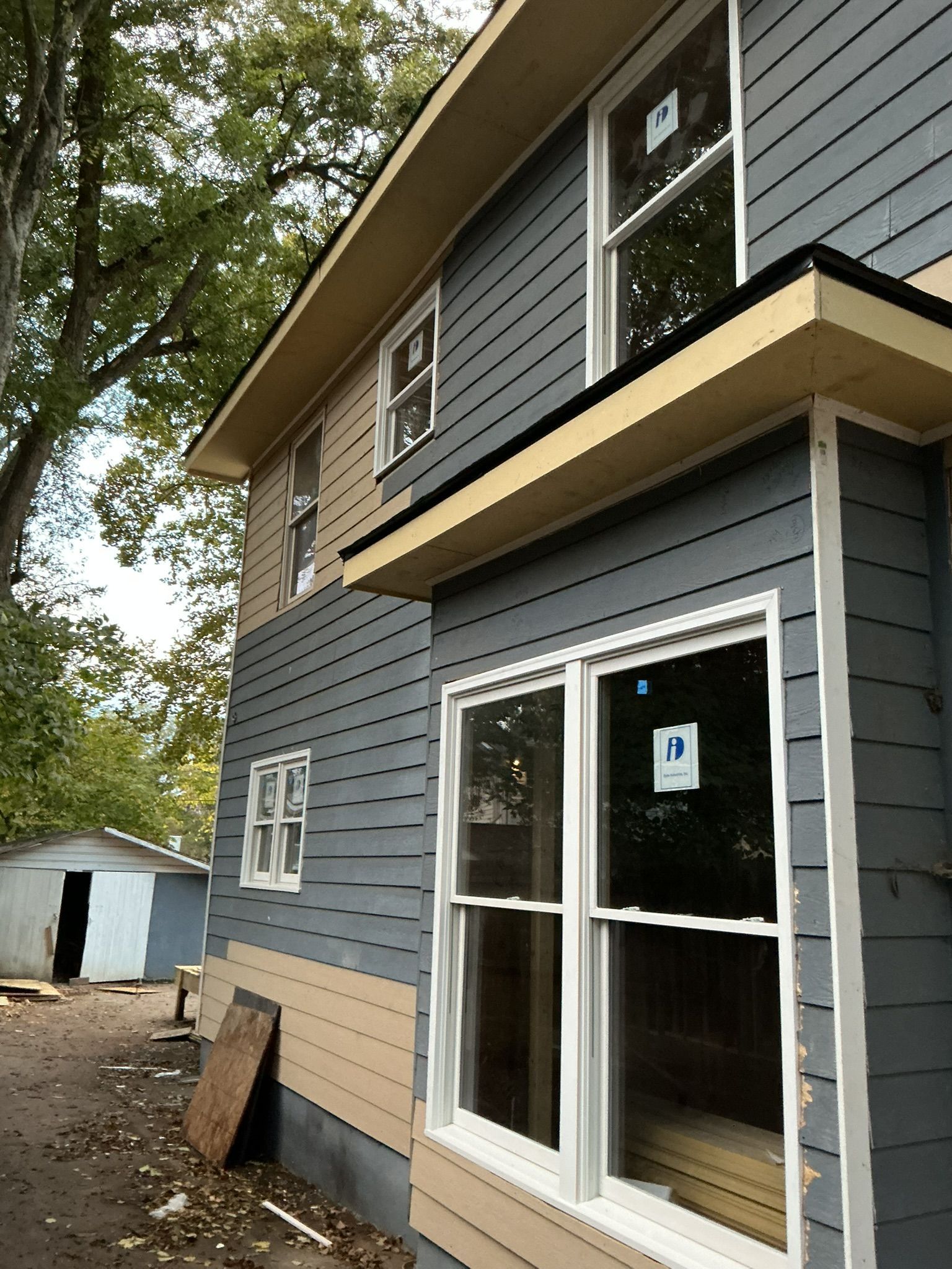 Two-story gray house with white trim and large windows, viewed from the side during construction.