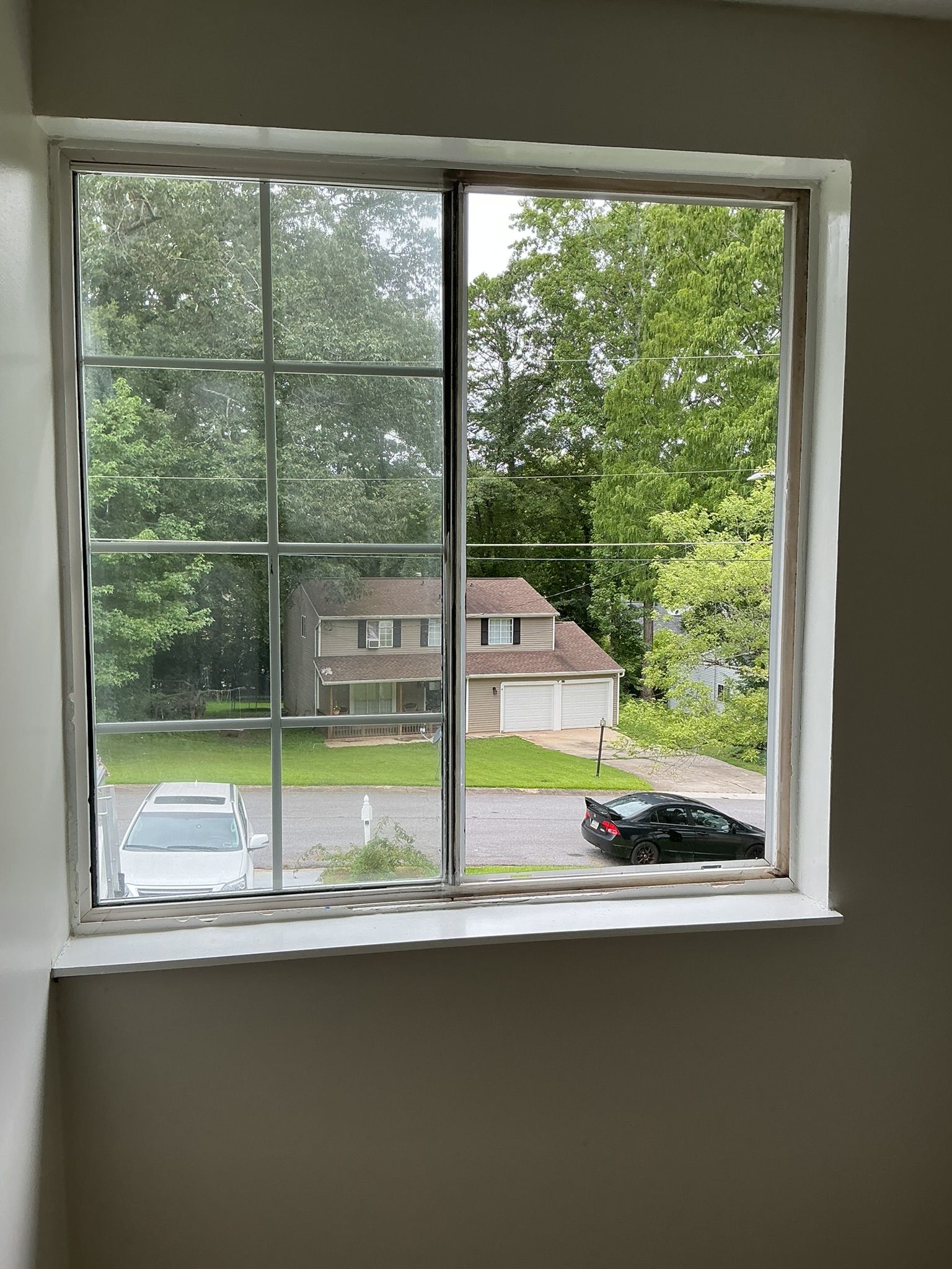 View from a window to parked cars, trees, and a house across the street.
