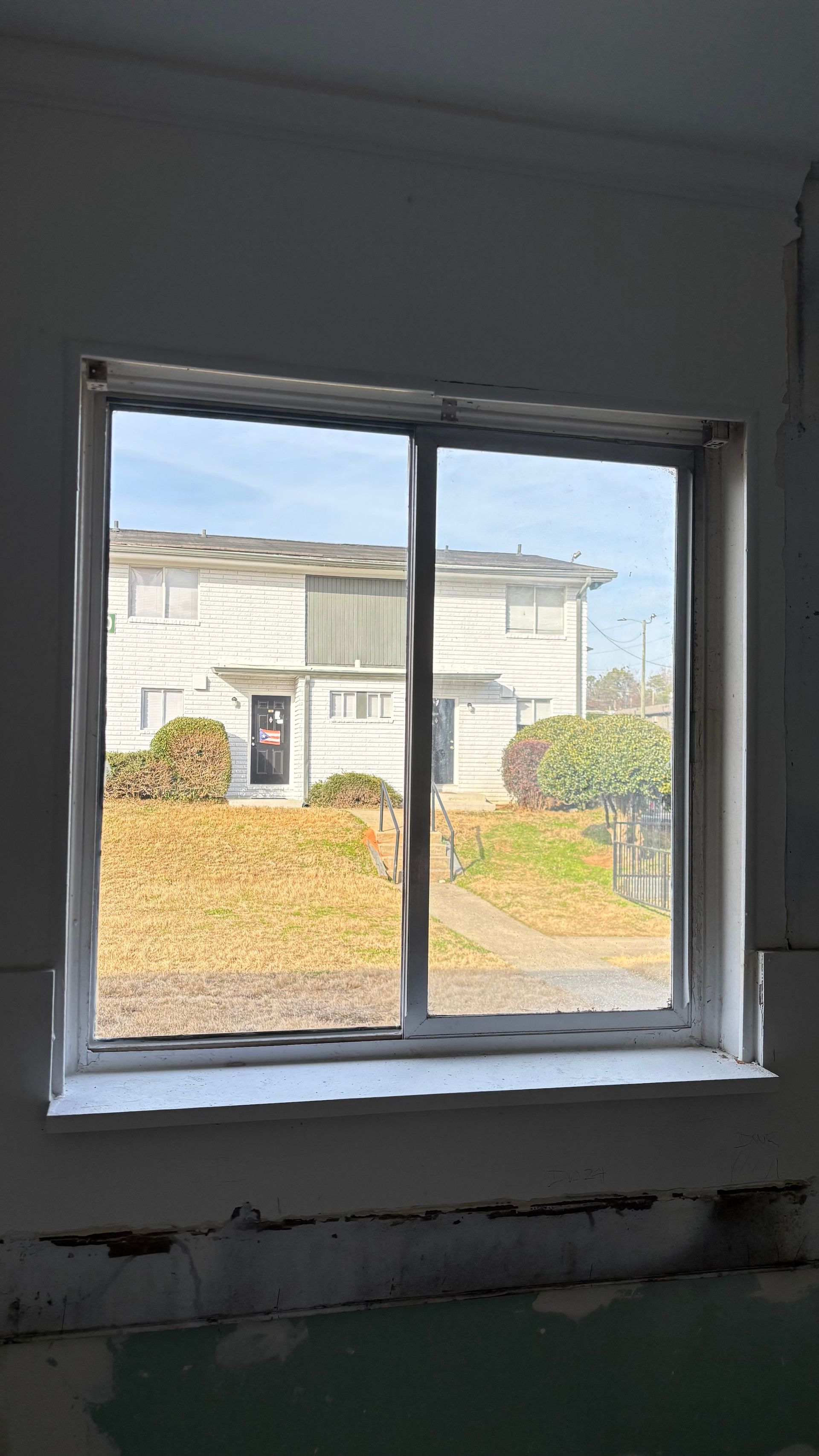 View through a window of a house across a yard with autumn leaves and blue sky