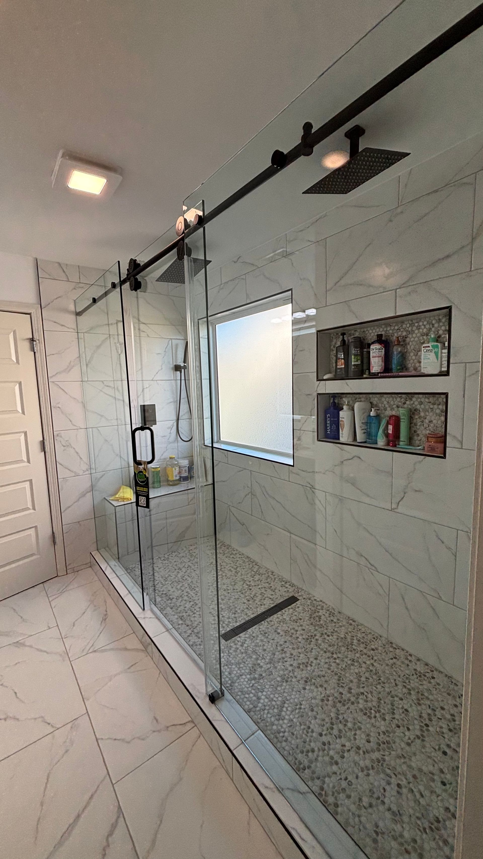 Glass shower enclosure in a bright tiled bathroom with a built-in shelf of toiletries.