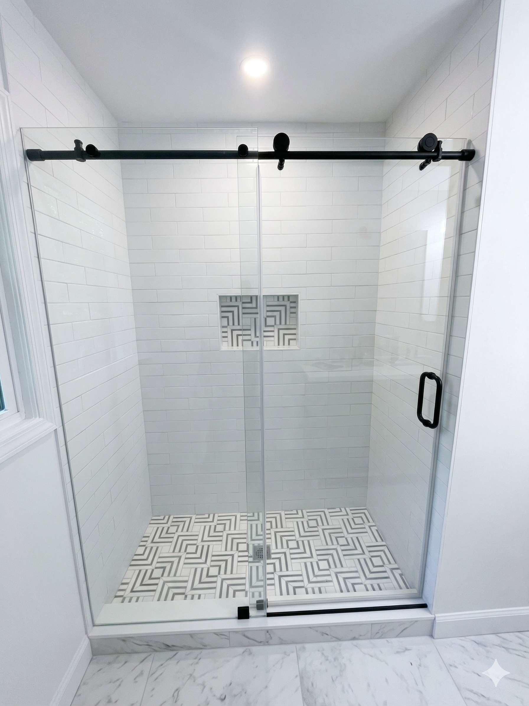 Empty white-tiled walk-in shower with black sliding door hardware and geometric floor tile.