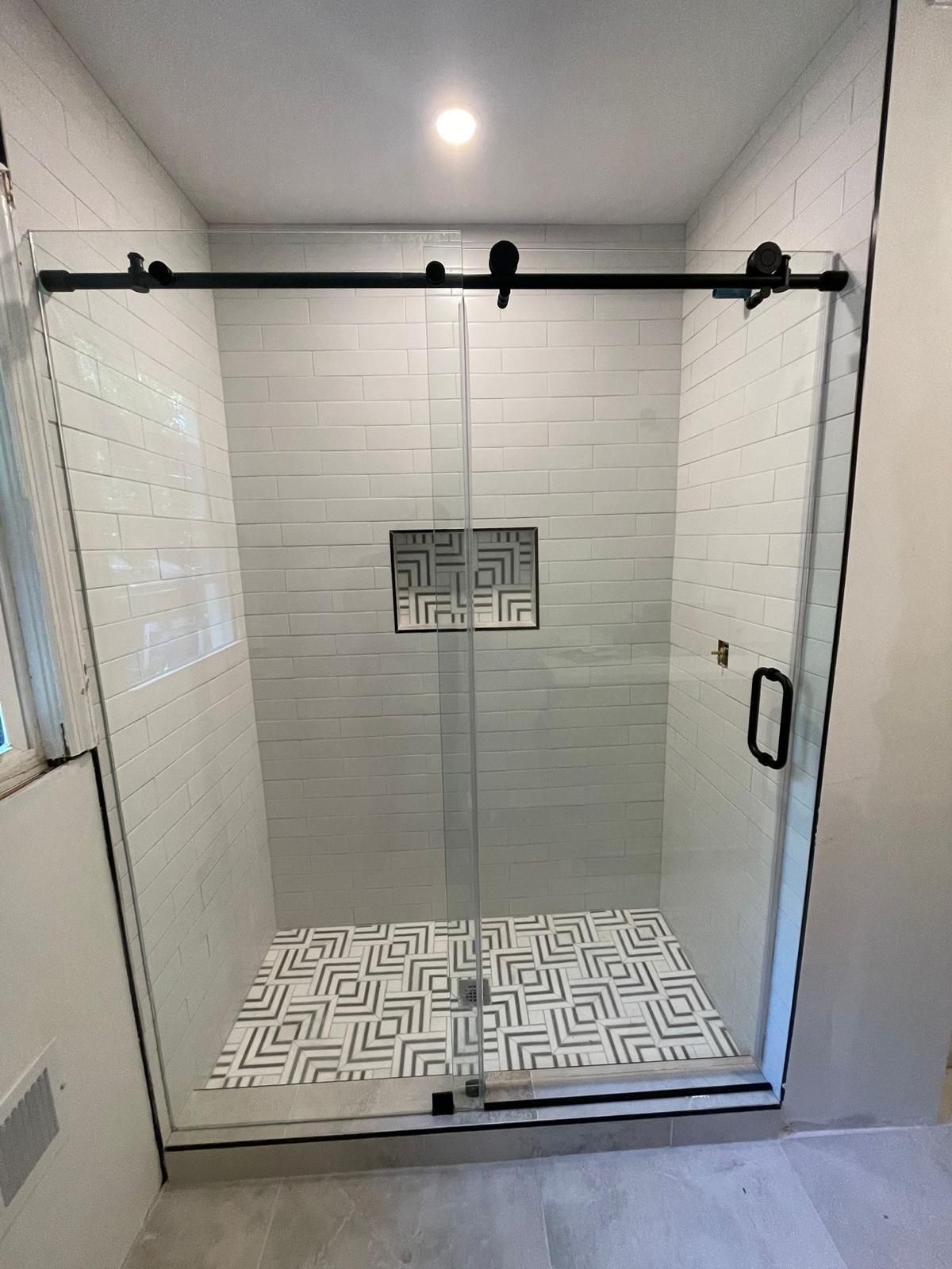 Small tiled walk-in shower with patterned floor and black sliding door hardware