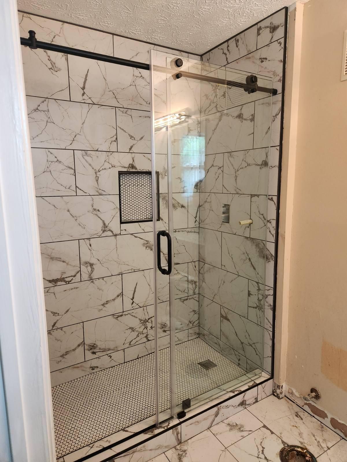 Modern bathroom with a glass walk-in shower, marble-look tile, and a pebble shower floor.