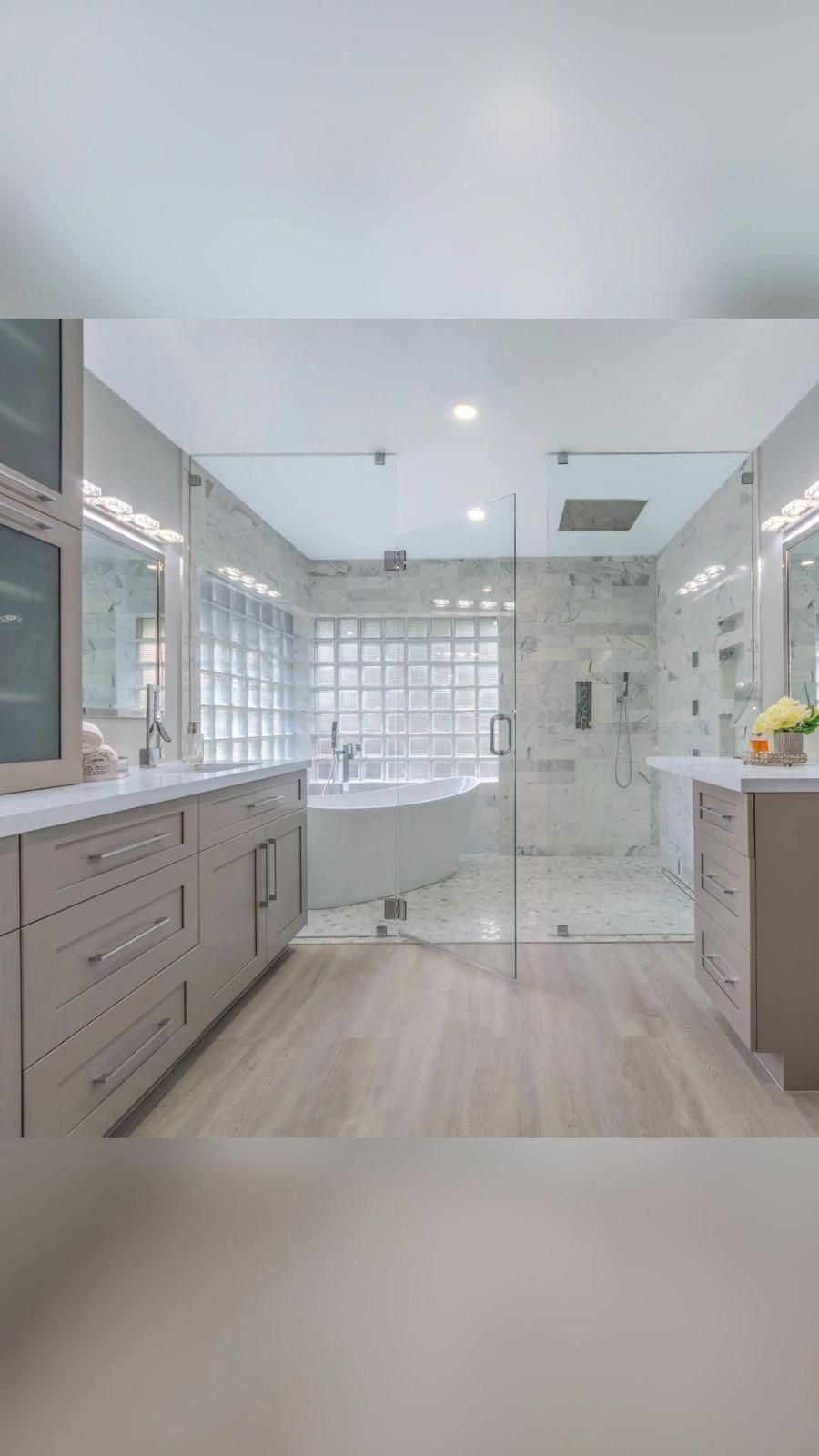 Bright modern bathroom with glass shower, large windows, and white-gray cabinetry