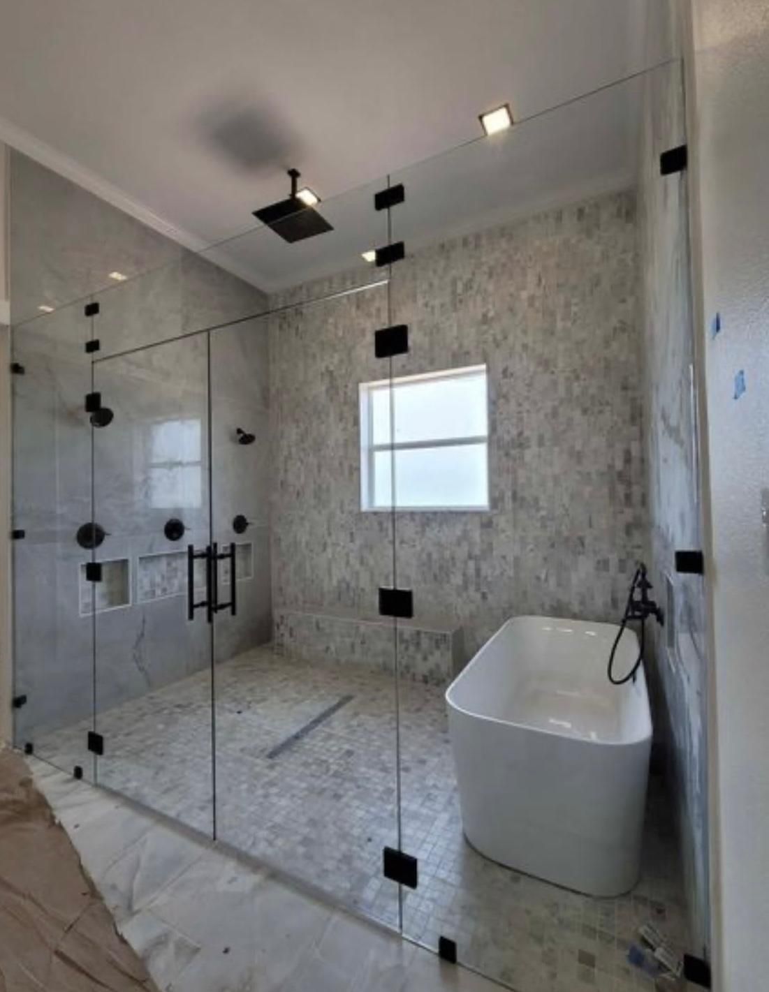 Modern tiled bathroom with glass shower, freestanding tub, and window