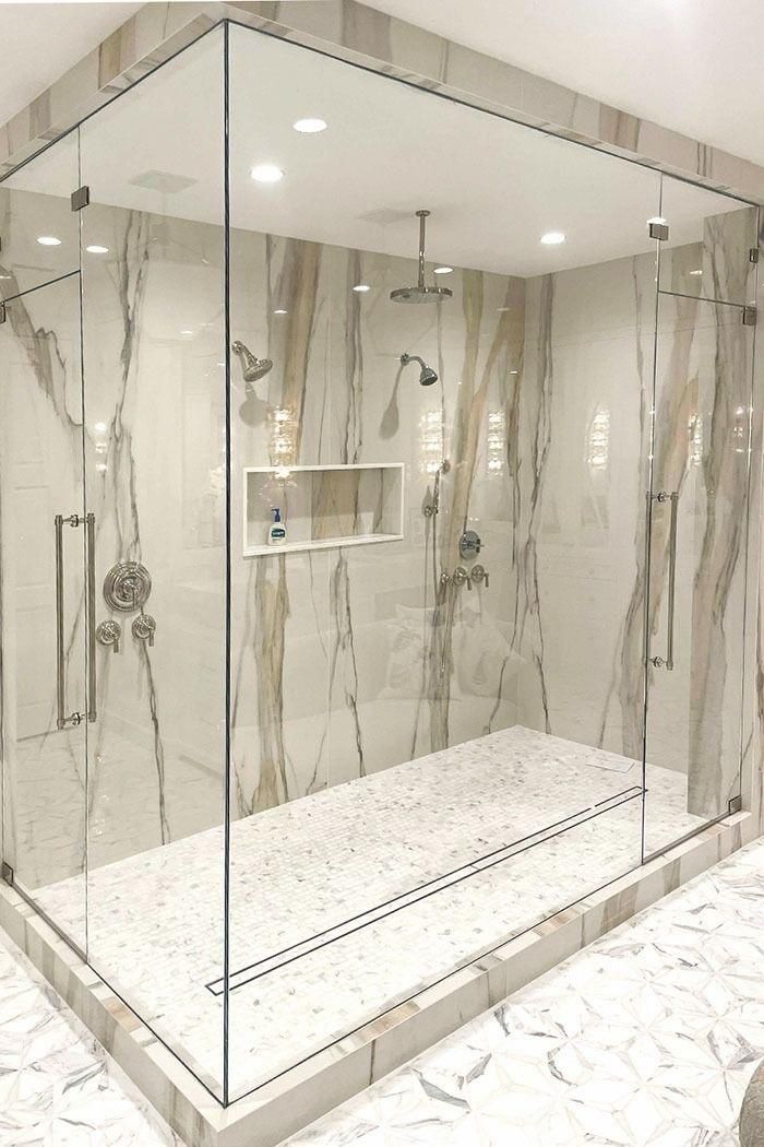 Glass shower enclosure with marble-look tile, rainfall showerheads, and white bench in a modern bathroom