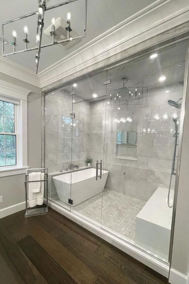 Bright bathroom with freestanding tub, large mirror, marble walls, and dark wood floor.