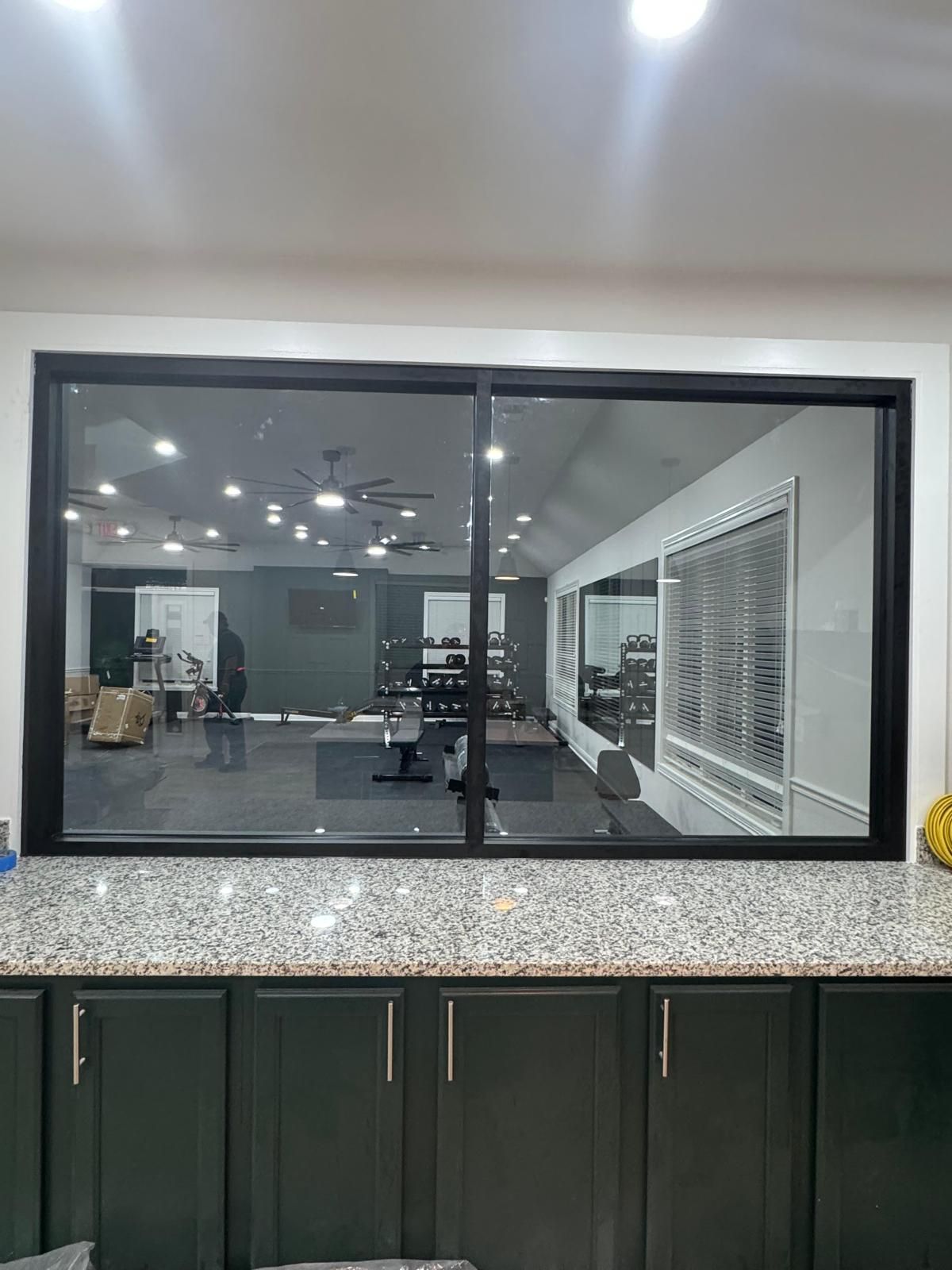 Modern office lobby with a large black-framed window, dark cabinets, and speckled countertop under ceiling lights