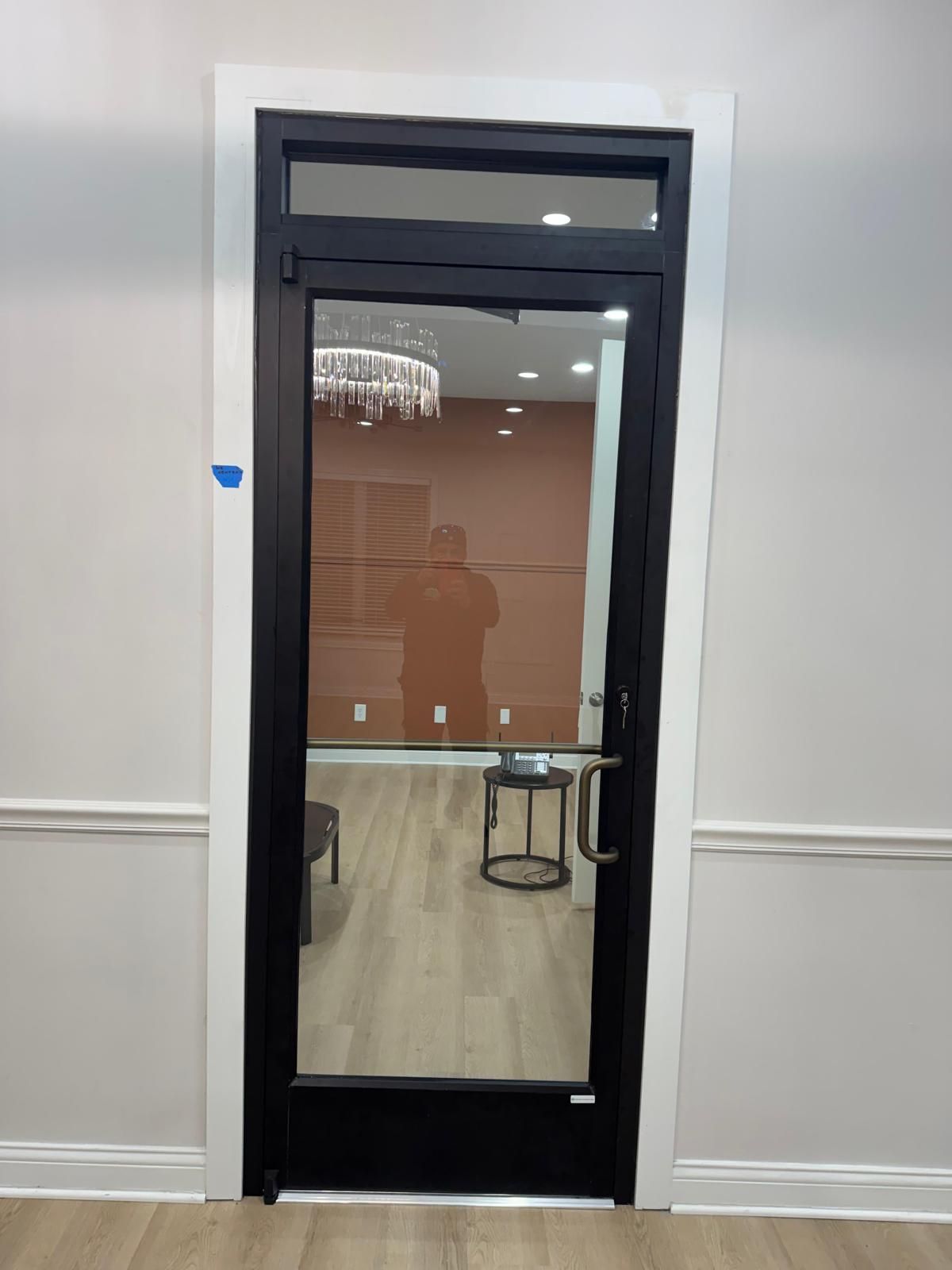 Black-framed glass door in a white hallway with a room visible through it.