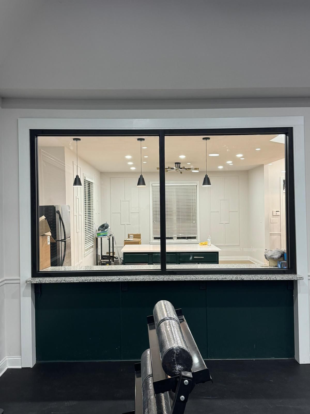 Wide interior view through a pass-through window into a bright kitchen with white cabinets and pendant lights.