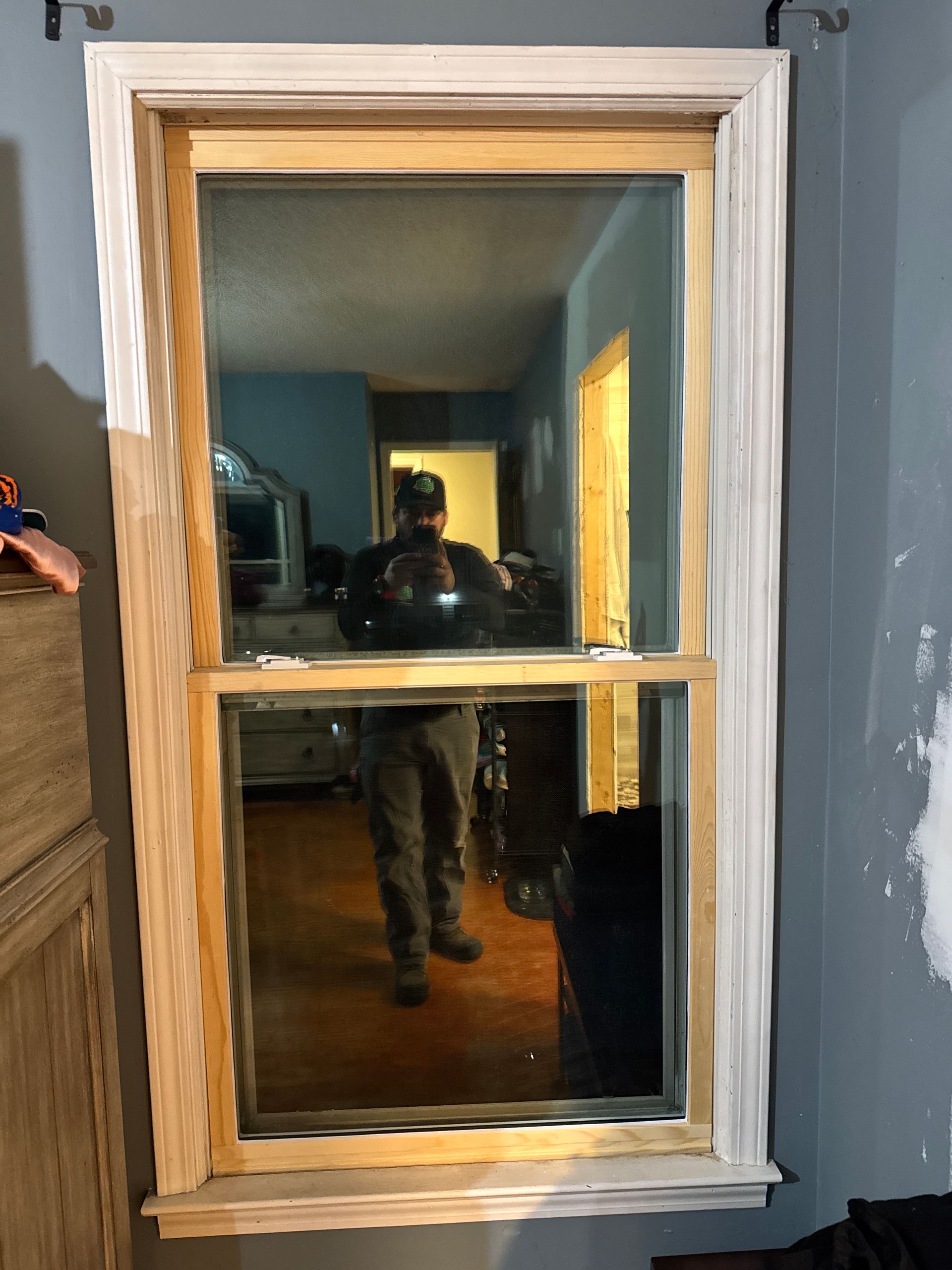 White-trimmed window on a dark blue wall, reflecting a room and a person holding the camera.